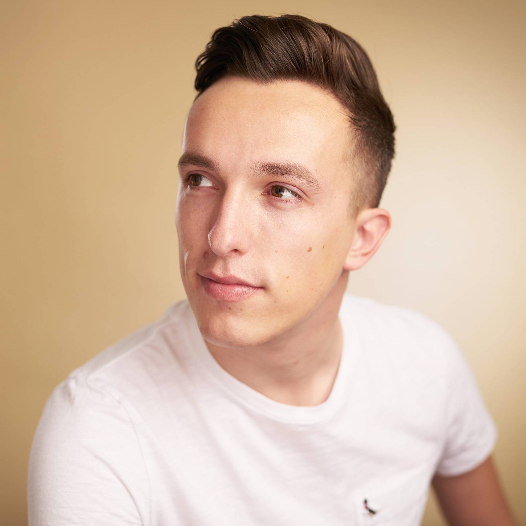 Photograph of Ben Tomlin in a white tshirt on a photography background looking to the side